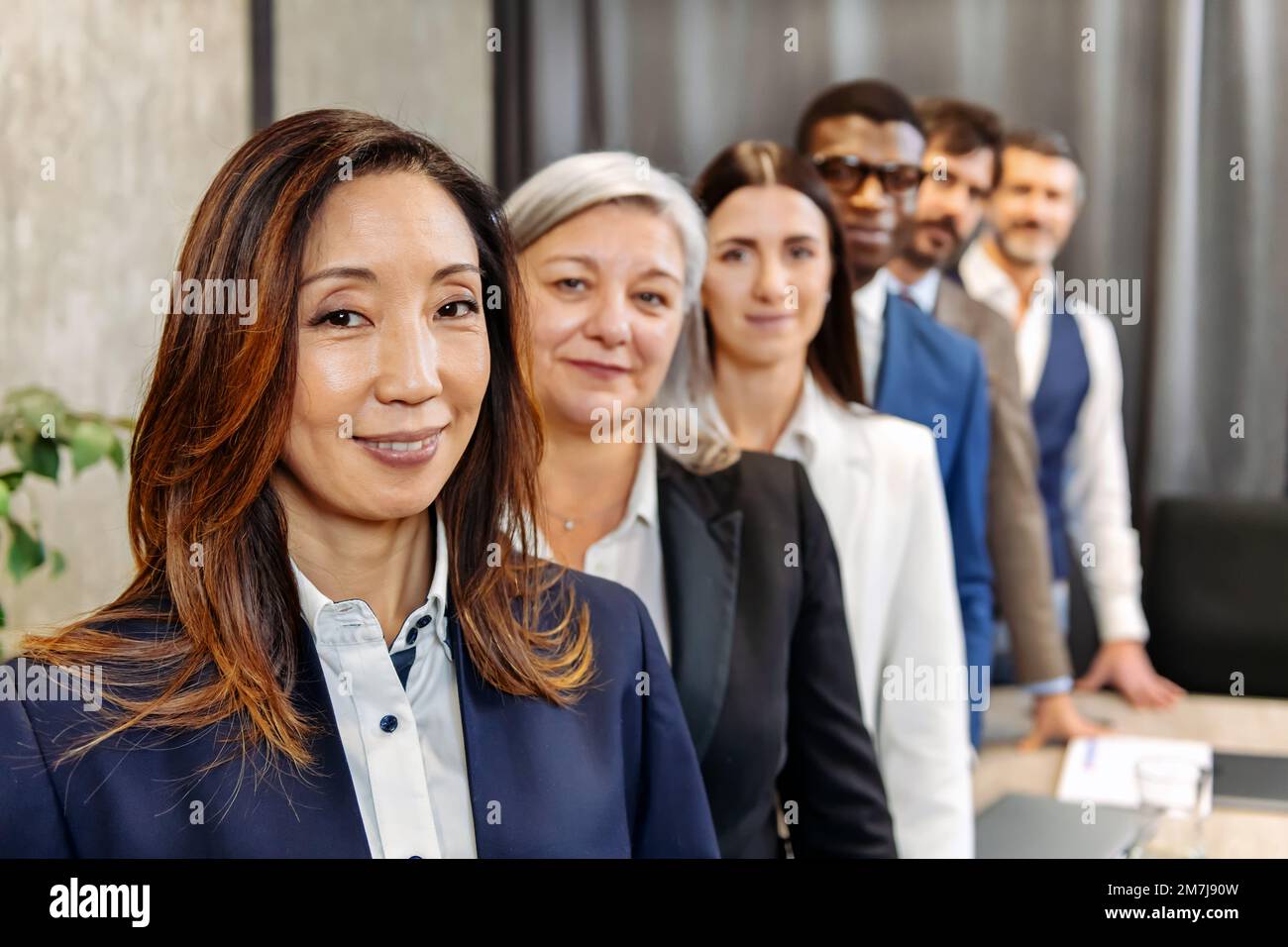 Une équipe composée de divers collègues en tenue habillée debout dans la rangée et regardant la caméra dans un bureau moderne Banque D'Images