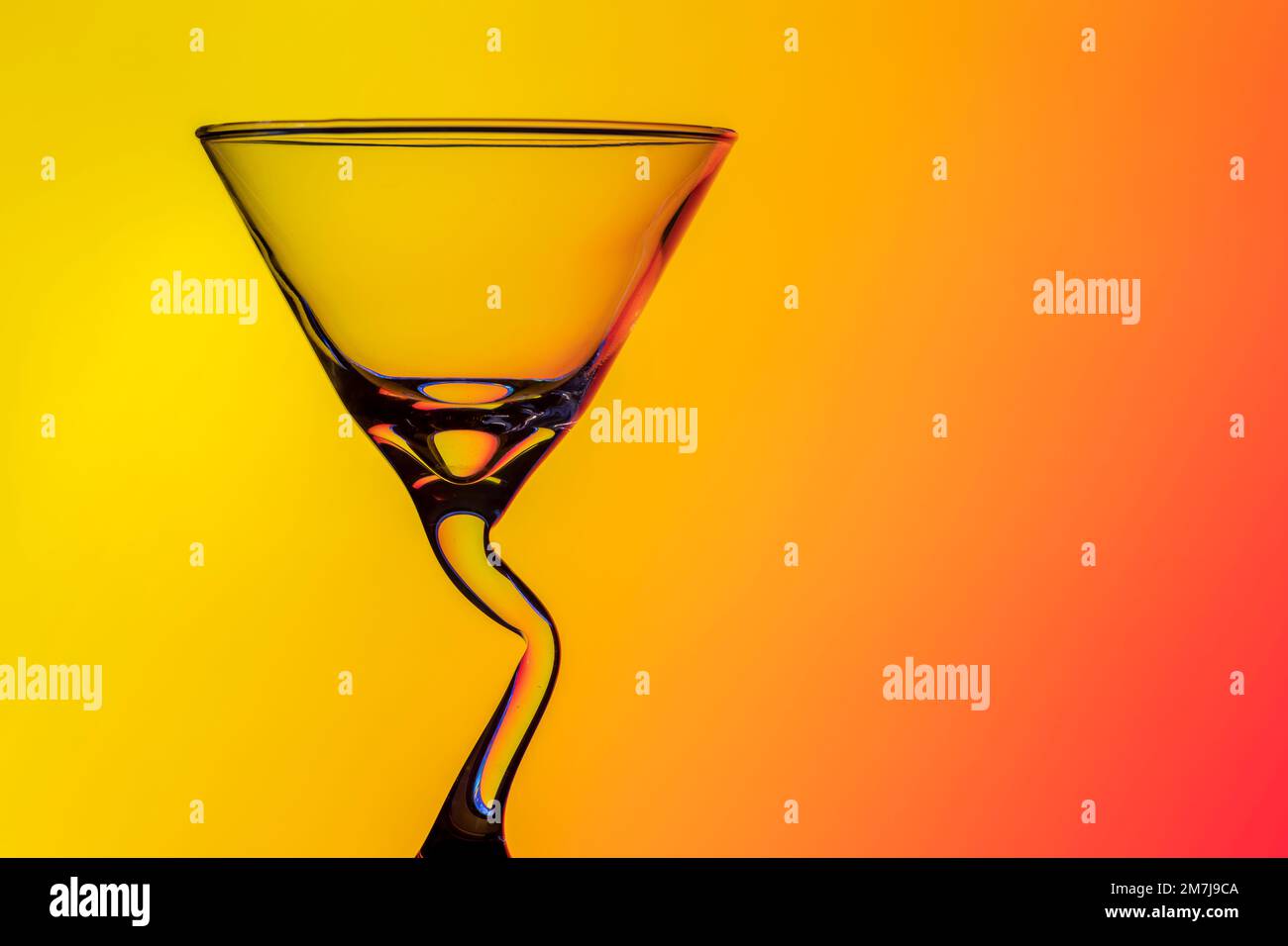 Magnifique verre à cocktail conique avec une tige en forme de bendy inhabituelle, photographié sur fond coloré produisant un motif de diffraction Banque D'Images