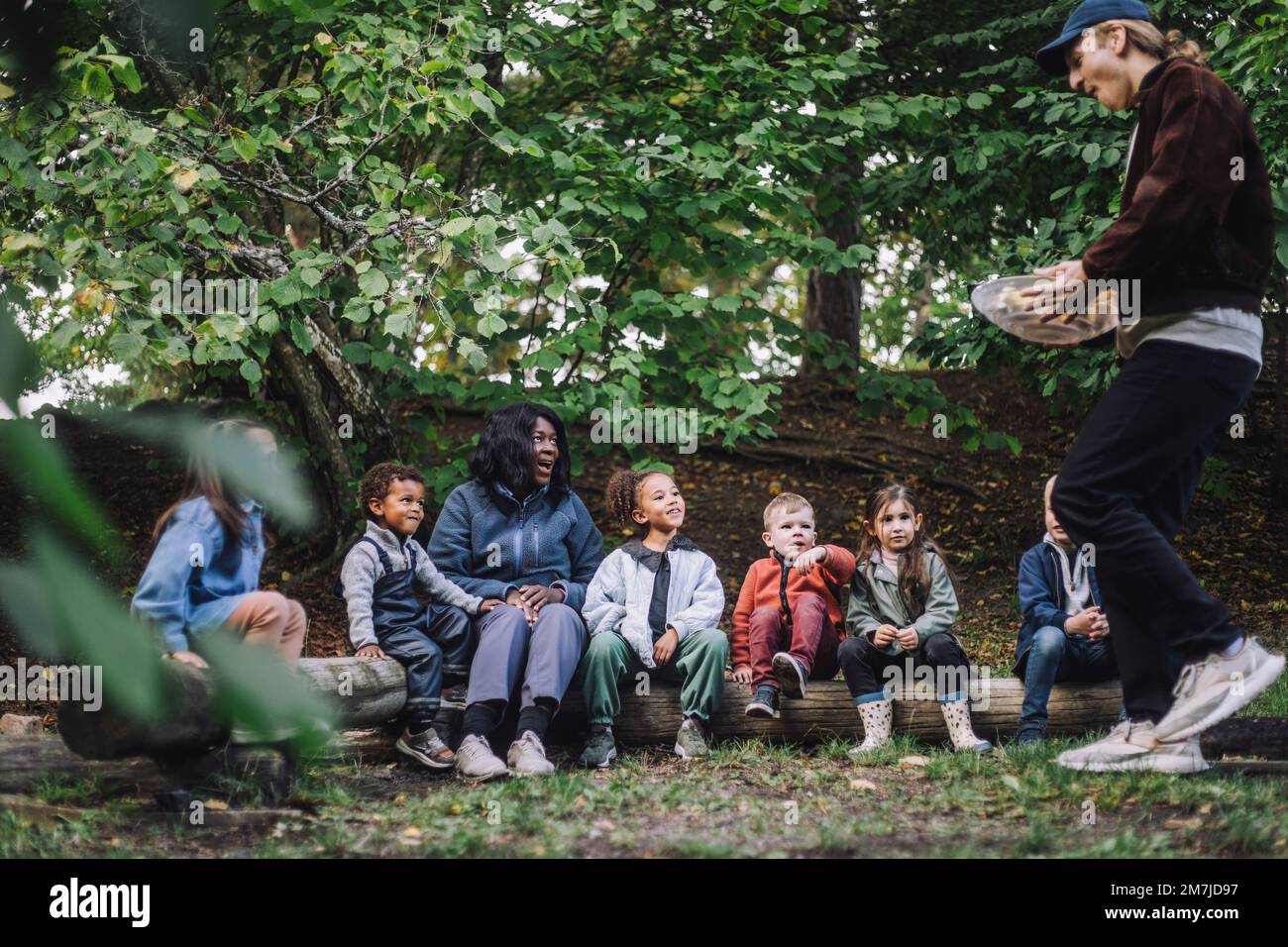 Une enseignante et des enfants d'âge préscolaire qui s'occupent de la garde d'enfants et qui leur servent de la nourriture dans le parc Banque D'Images