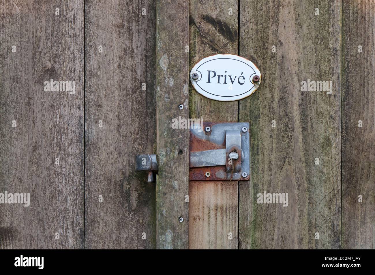 Gros plan de la vieille porte de clôture en bois avec poignée en métal rouillé et panneau de propriété privée ovale blanc avec texte privé en néerlandais. Banque D'Images