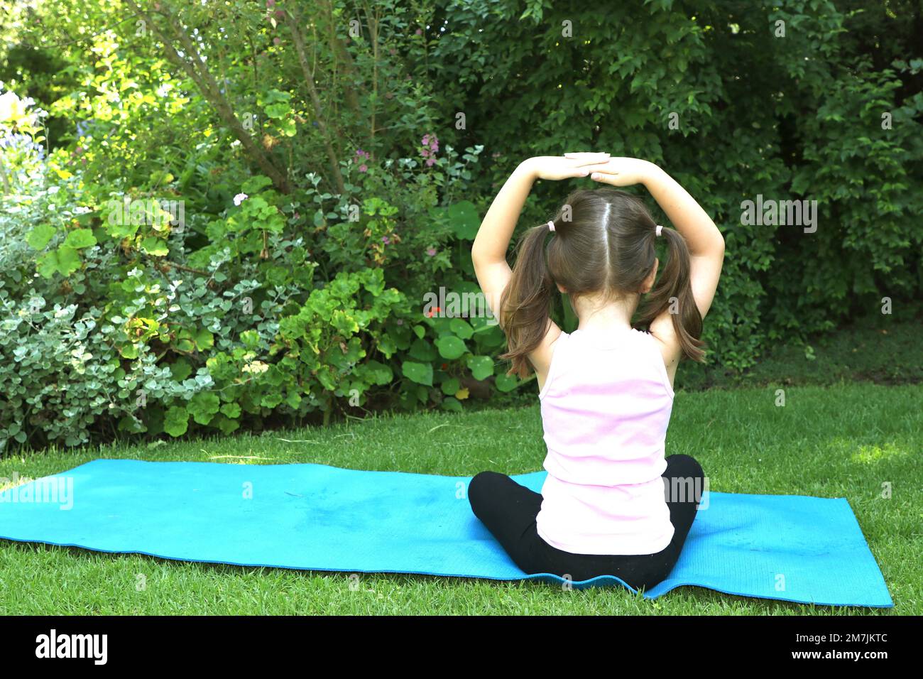 Une jeune fille de 7-10 ans faisant du yoga pose dans le jardin portant des picots sur un tapis de yoga bleu Banque D'Images