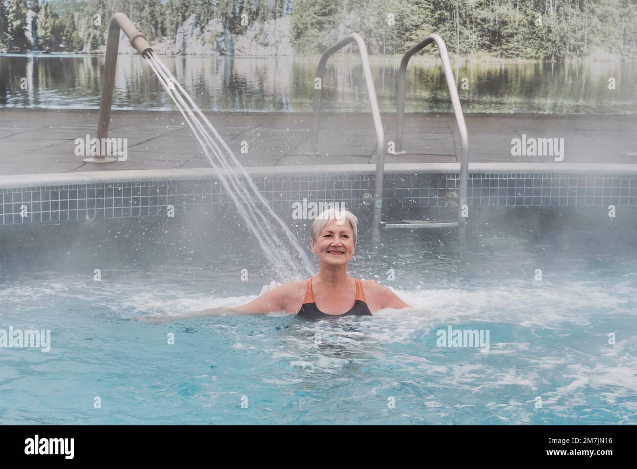 Bonne femme blanche mûre souriante avec cheveux courts gris dans la piscine thermale extérieure avec hydromassage. Concept des aînés actifs. Banque D'Images