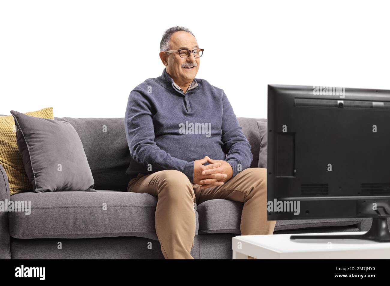 Homme mûr souriant assis sur un canapé et regardant la télévision isolée sur fond blanc Banque D'Images