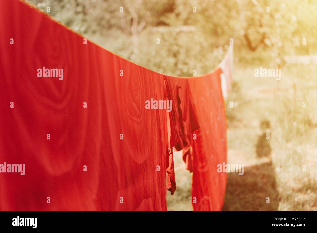 le linge de lit rouge est séché sur une corde à linge dans la rue dans la cour de la maison de campagne du village. été, fraîcheur et jour de blanchisserie. chore homewo Banque D'Images