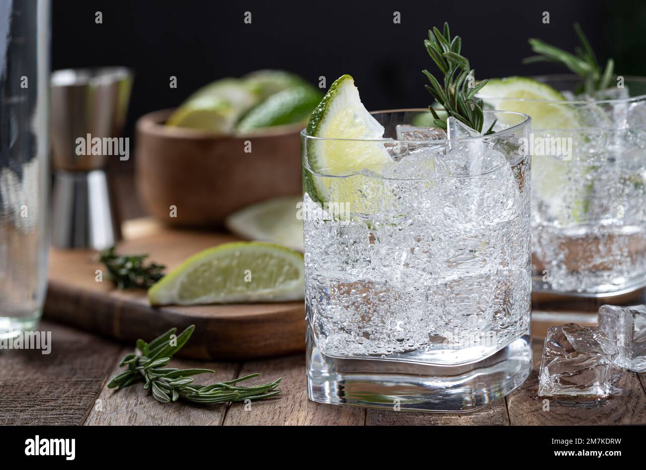 Gin et cocktail tonique avec des tranches de citron vert, du romarin et de la glace sur une table rustique en bois Banque D'Images