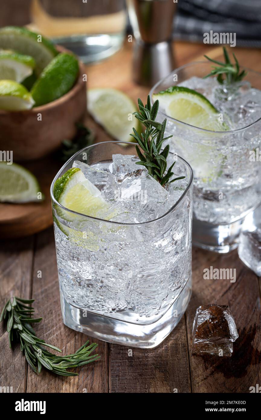 Gin et cocktail tonique avec des tranches de citron vert, du romarin et de la glace sur une table rustique en bois Banque D'Images