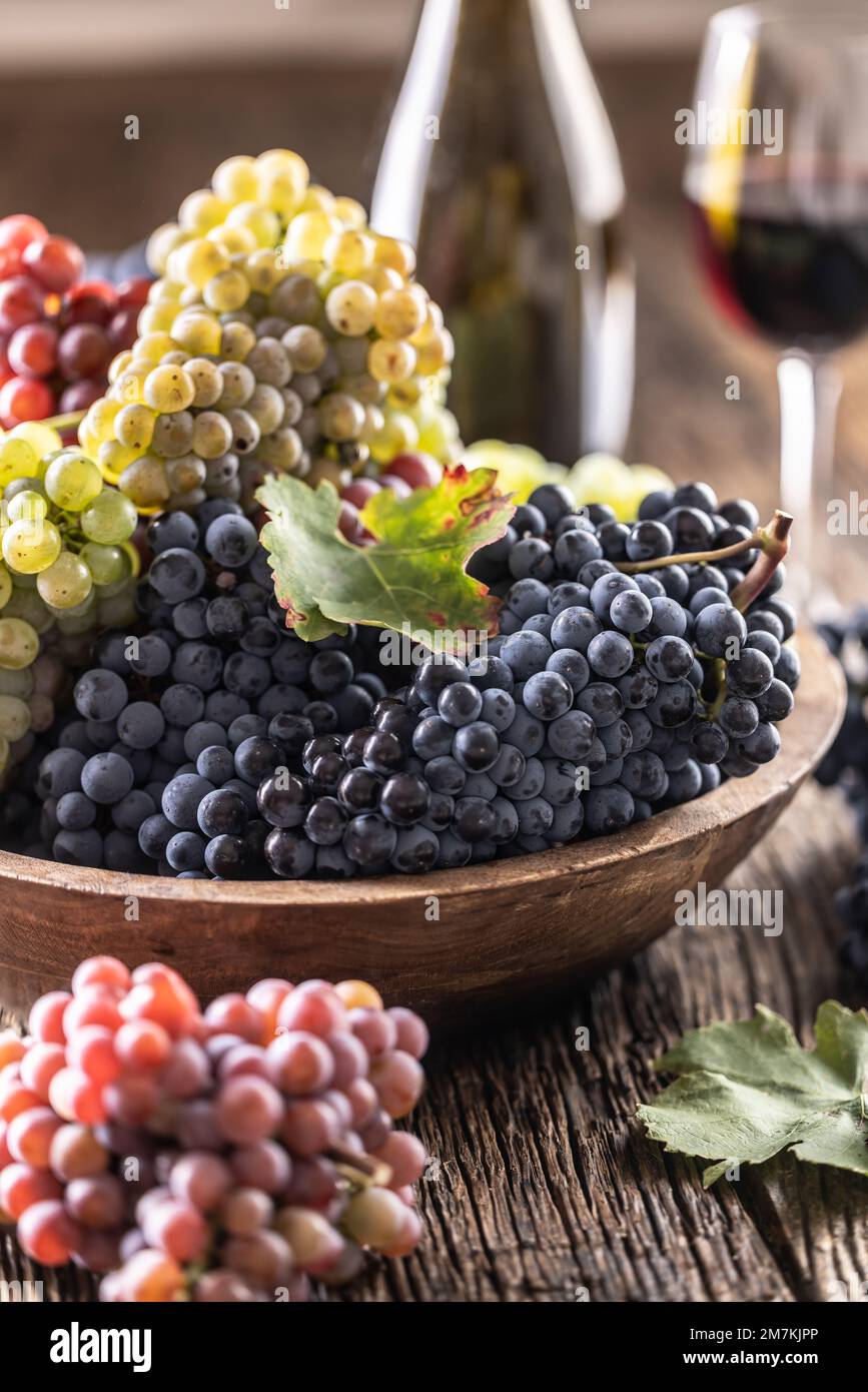 Des petits pains juteux de raisins dans un bol en bois, du vin rouge en arrière-plan. Banque D'Images