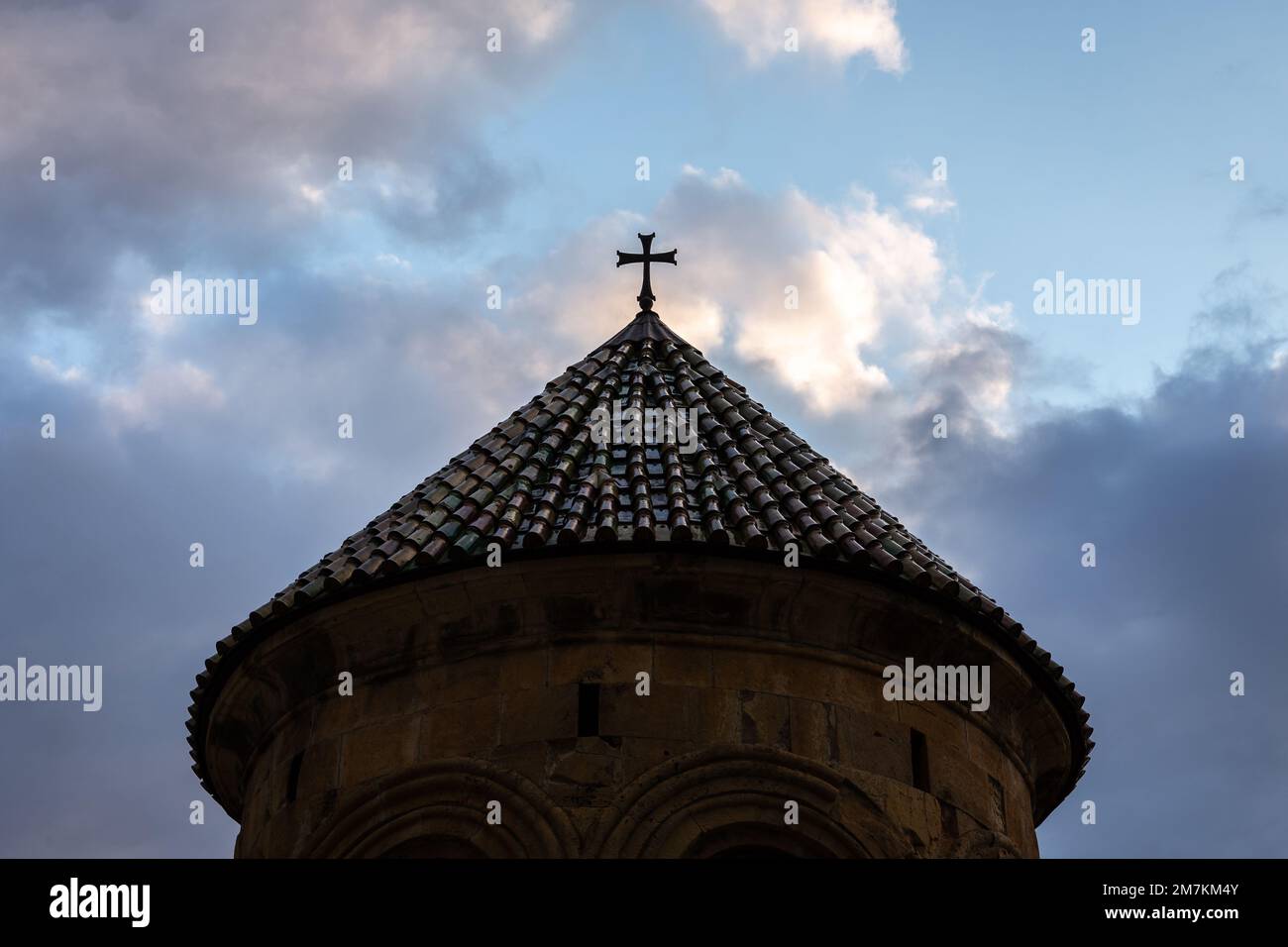 Belfry du monastère de la Gelati (clocher) silhouette sombre sur ciel bleu ciel nuageux, vue symétrique avec toit en tuiles vertes et croix sur le dessus. Banque D'Images