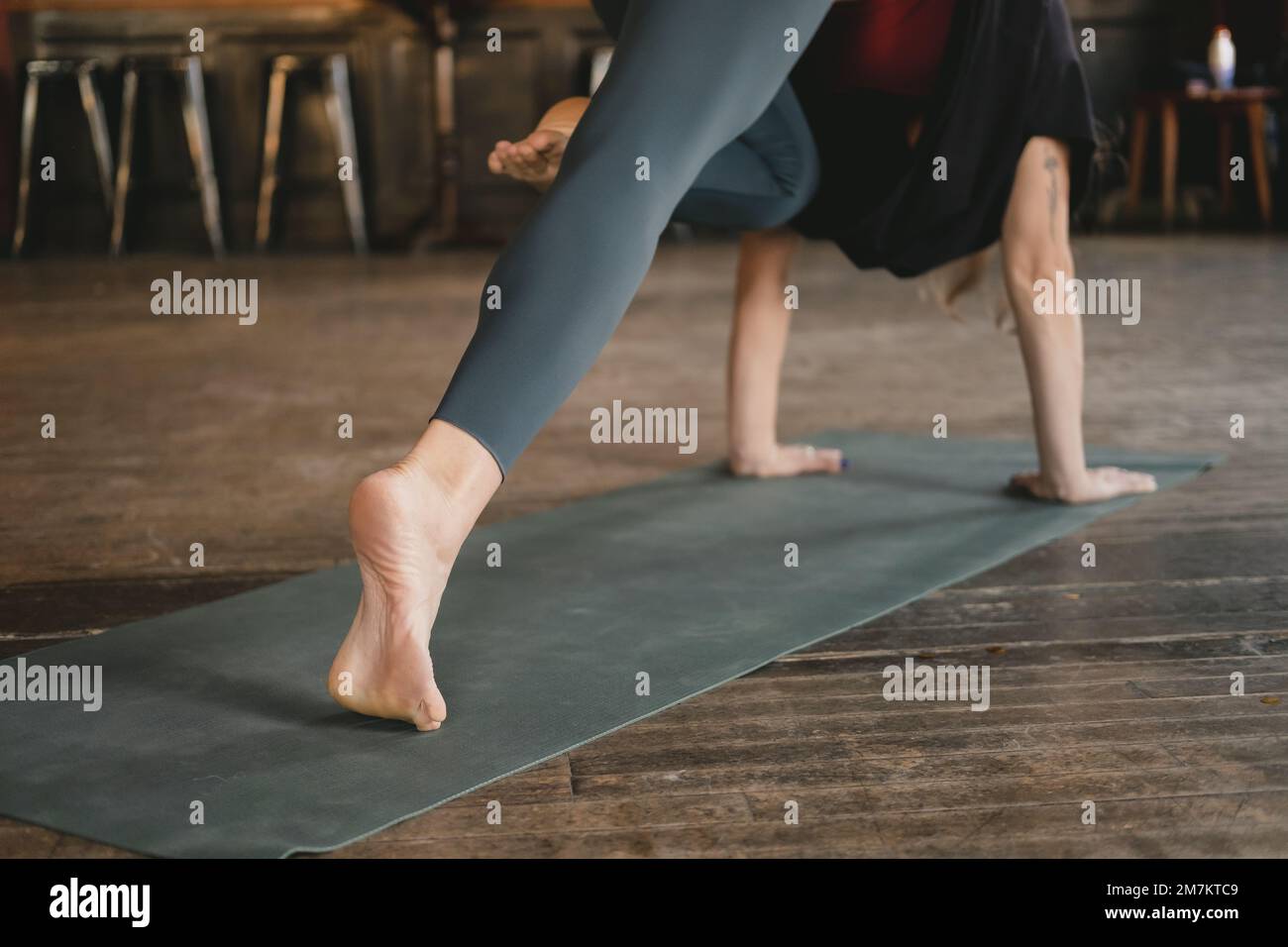 Femme non reconnaissable yogi nouveau professeur faisant un chien à trois pattes face vers le bas pose genou à nez, entraînement de yoga, pieds nus et portant des sportswe Banque D'Images