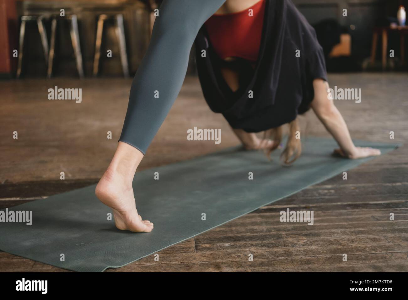 Femme yogi méconnaissable et nouveau professeur faisant une posture de chien à trois pattes face au sol, entraînement au yoga, pieds nus et portant des vêtements de sport Banque D'Images
