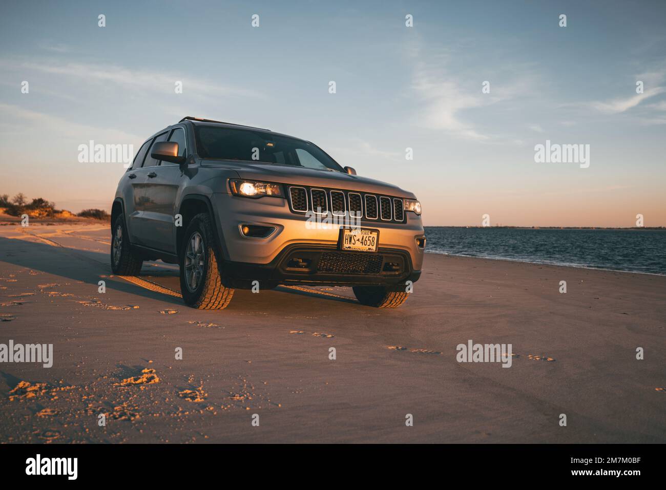 Un Jeep Grand Cherokee gris 2018 à la plage au coucher du soleil Banque D'Images