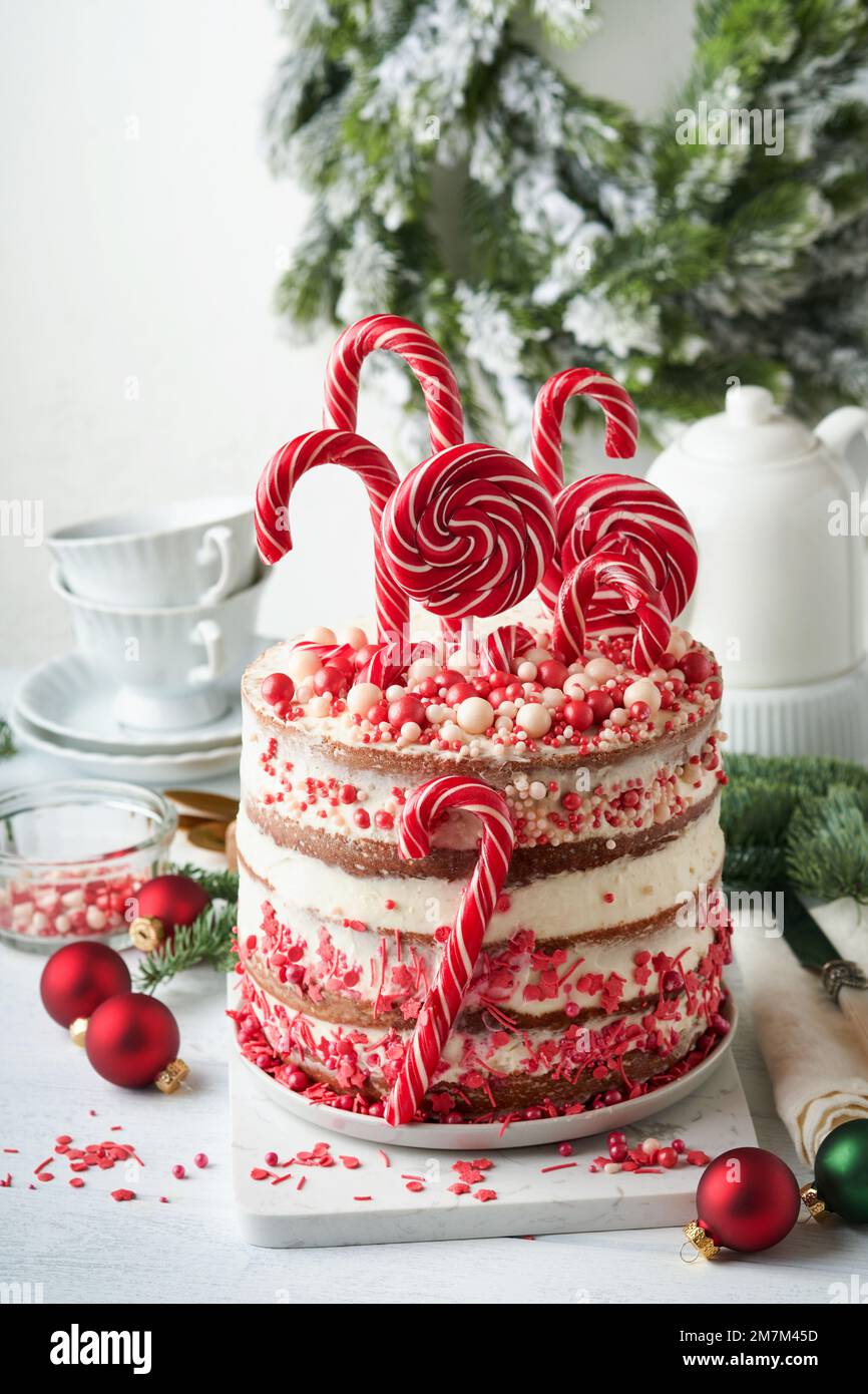 Noël de nombreuses couches de gâteau décoré avec des pop lolli, confetti rouge et blanc sur support à gâteau blanc, boules de Noël, branches de sapin sur tabl de béton blanc Banque D'Images