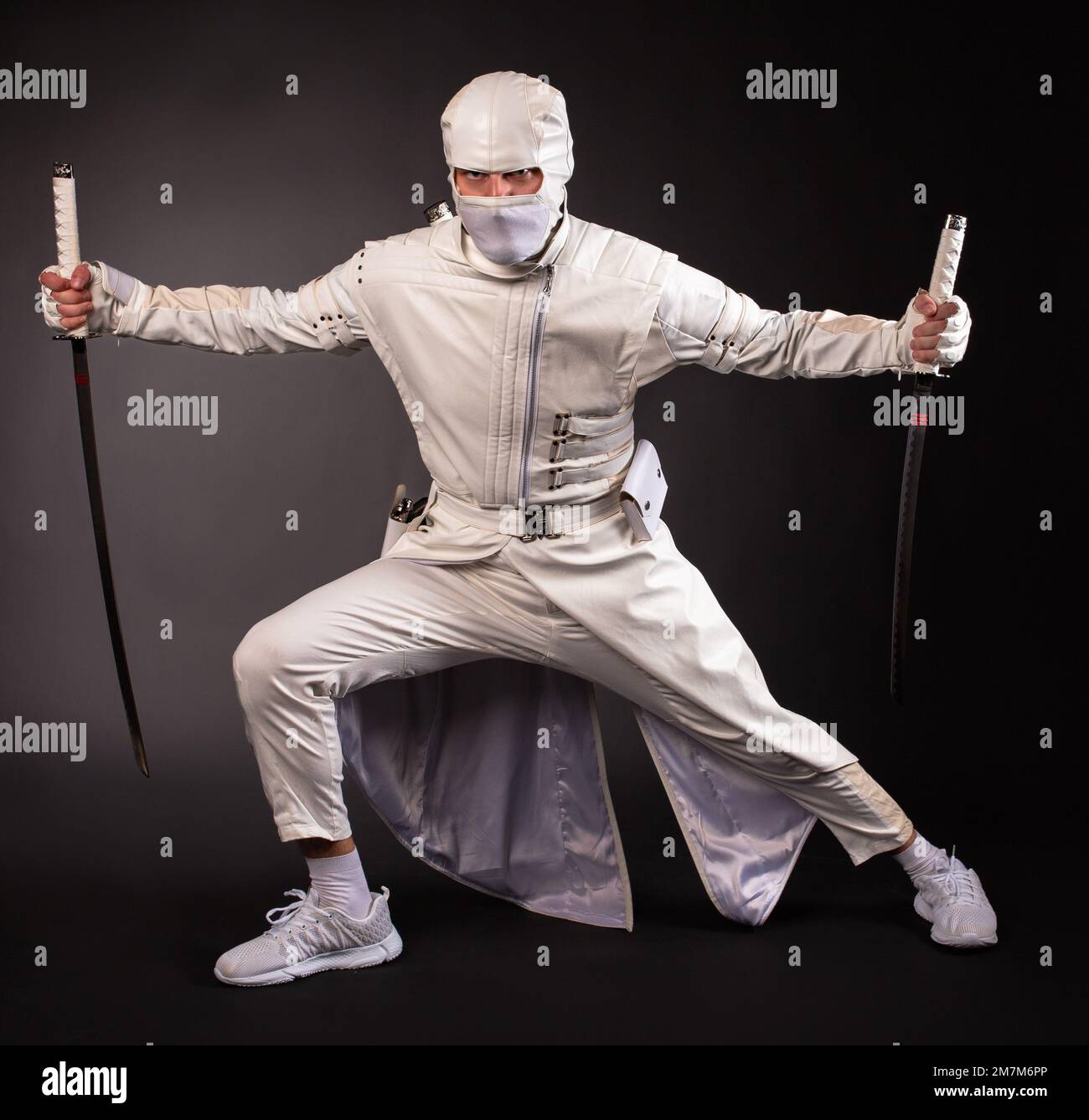 Un homme sous la forme d'un ninja de combat pose avec deux épées sur un fond noir Banque D'Images