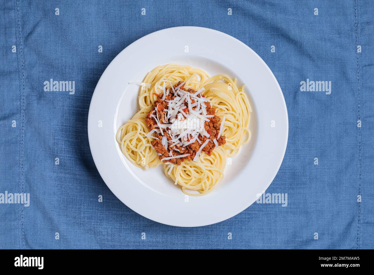 Spaghetti à la bolognaise avec parmesan sur une assiette blanche. Décor et arrière-plan bleus simples. Plats italiens traditionnels, cuisine méditerranéenne Banque D'Images