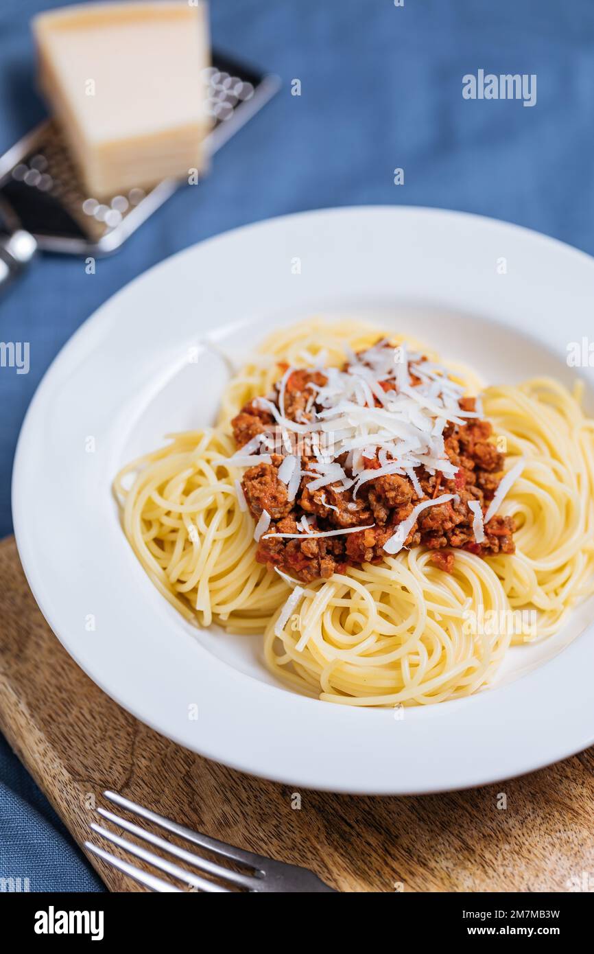 Spaghetti à la bolognaise avec parmesan sur une assiette blanche. Décor et arrière-plan bleus simples. Plats italiens traditionnels, cuisine méditerranéenne Banque D'Images