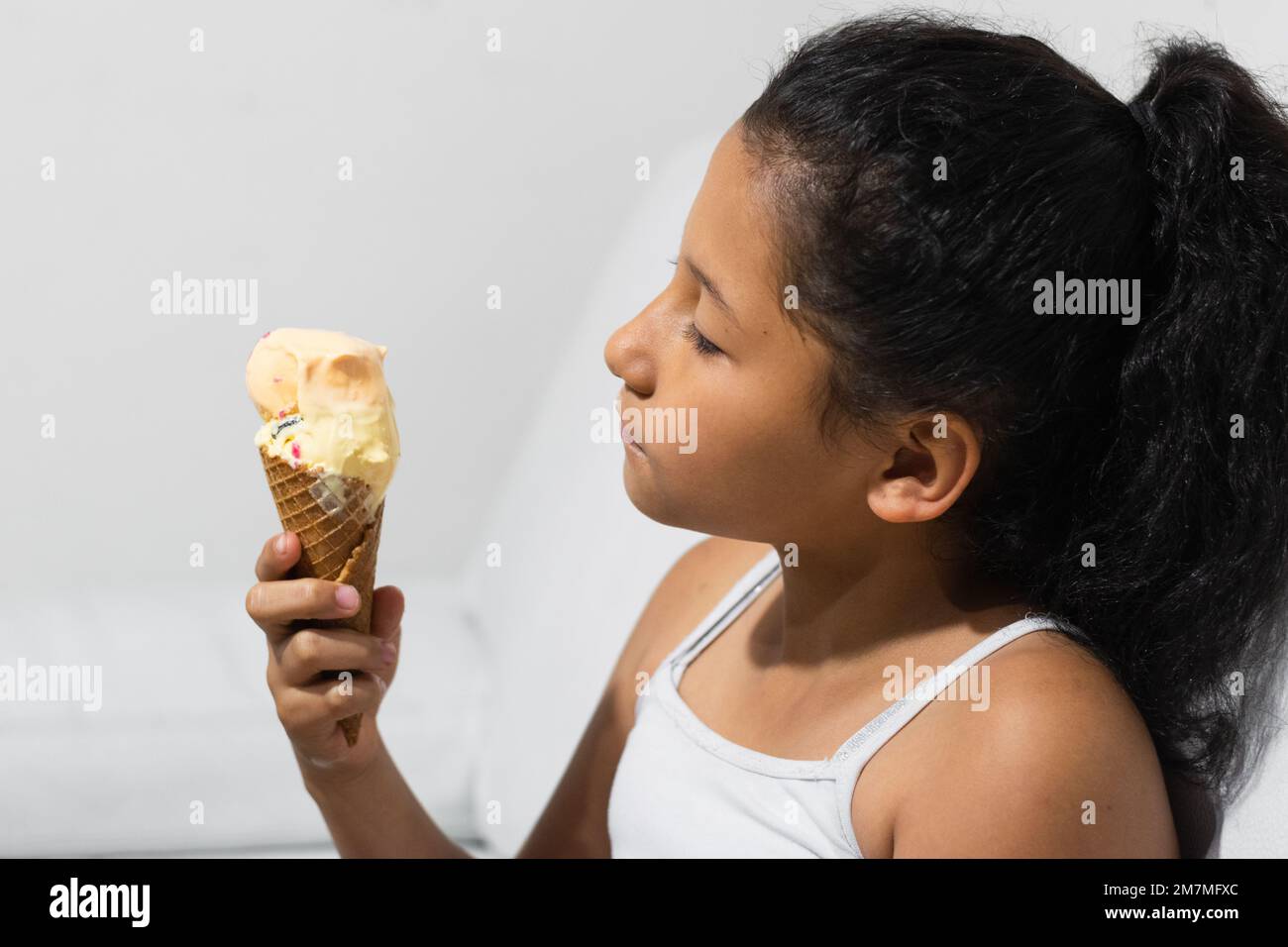 petite fille de latina à la peau brune, tenant un cône de crème glacée dans sa main, la regardant avant de la manger Banque D'Images