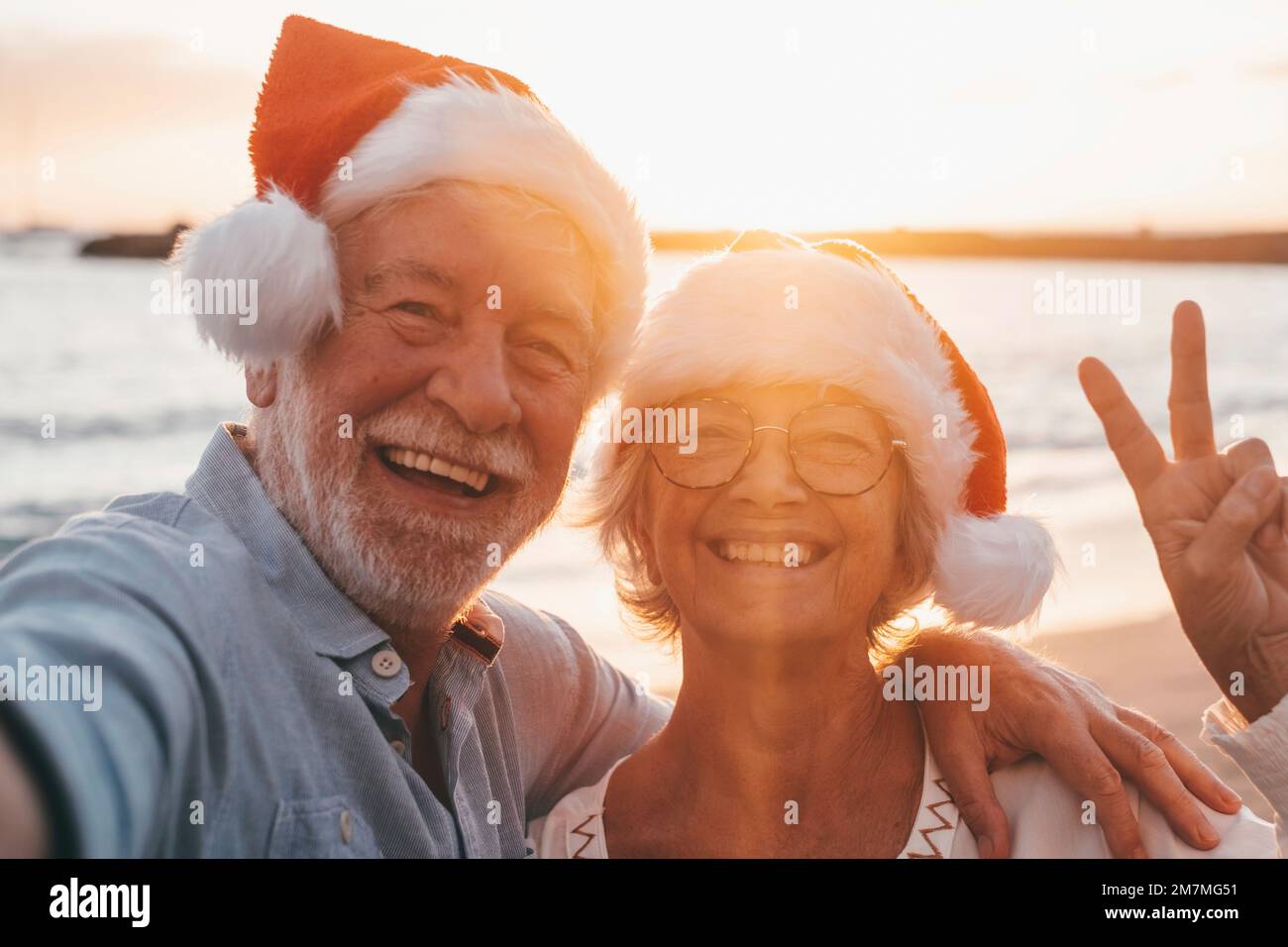 Portrait de deux personnes âgées mignonnes s'amusant et appréciant ensemble à la plage les jours de noël à la plage portant des chapeaux de Noël. Regarder et tenir un appareil photo prendre des vidéos de vacances Banque D'Images