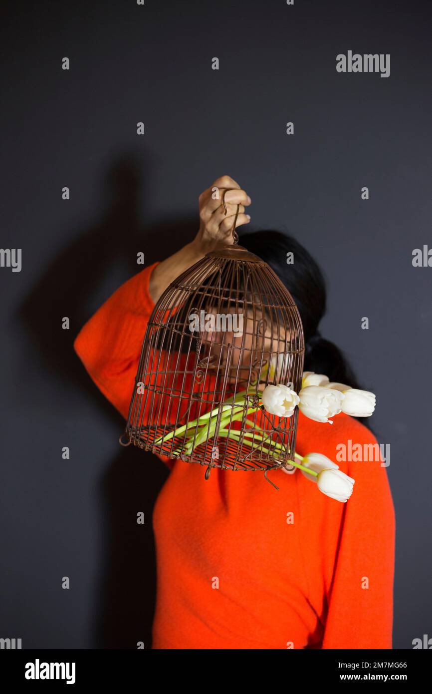 Femme aux cheveux foncés avec cage d'oiseau antique remplie de tulipes blanches Banque D'Images