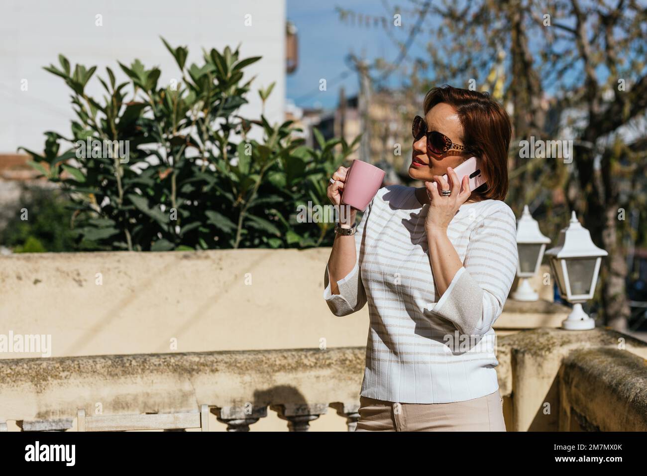 Femme avec des lunettes de soleil parlant au téléphone tout en se tenant  debout à l'extérieur dans une terrasse Photo Stock - Alamy
