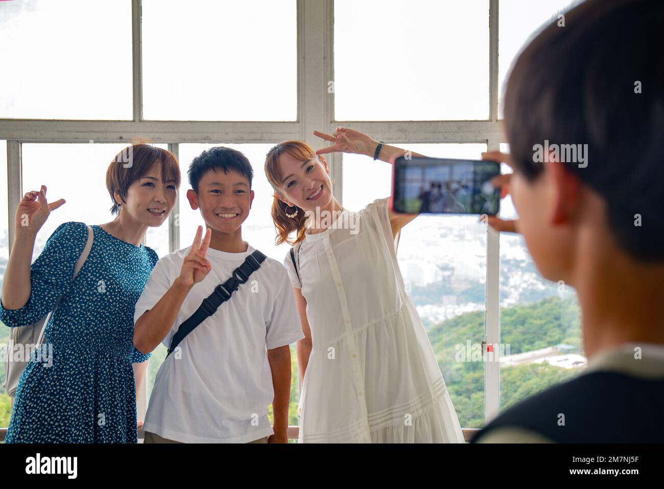 Un garçon utilisant son téléphone portable pour prendre une photo de trois personnes, un garçon de 13 ans, sa mère et un ami. Banque D'Images
