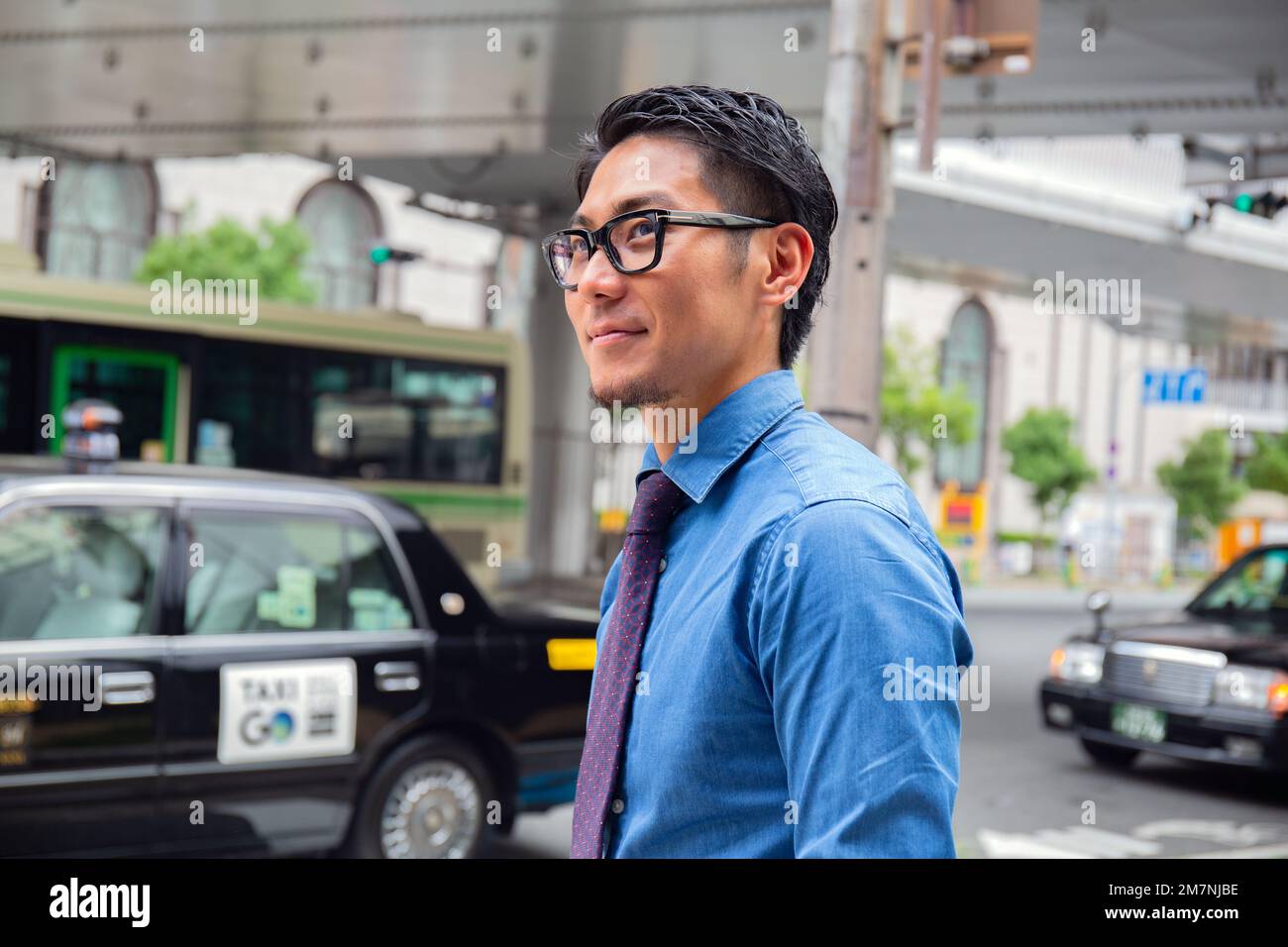 Un jeune homme d'affaires dans la ville, en déplacement, un homme dans une chemise bleue et cravate, un taxi derrière lui. Banque D'Images