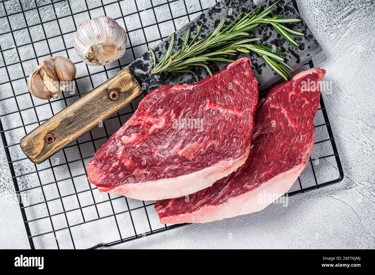 Steak de viande de bœuf de bœuf de bœuf cru sur un couperet de boucher, steak de bosse de chapeau. Arrière-plan blanc. Vue de dessus Banque D'Images