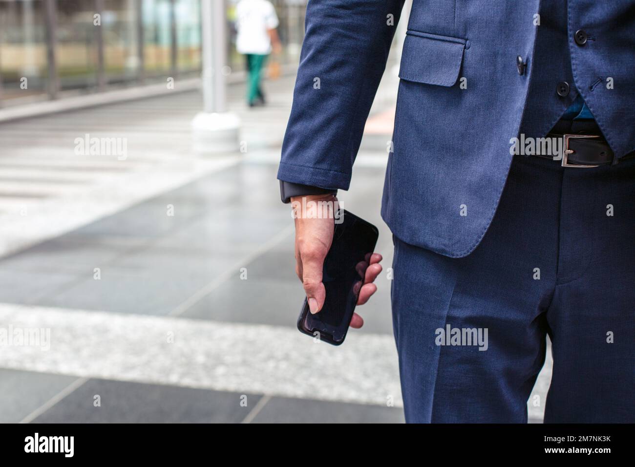 Un jeune homme d'affaires en costume bleu en déplacement dans un quartier du centre-ville, tenant son téléphone portable. Banque D'Images