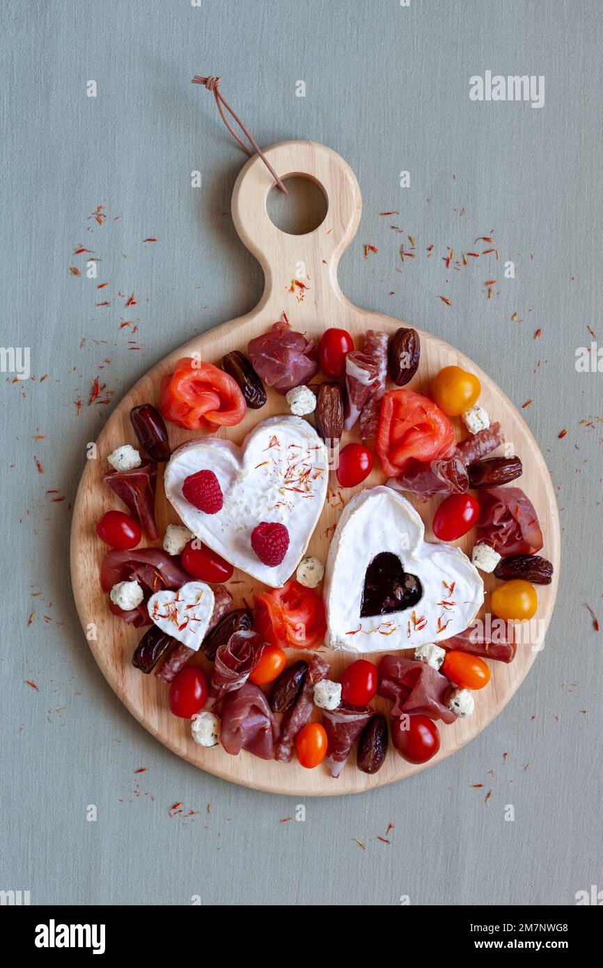 Plateau de fromages de la Saint-Valentin avec fromage en forme de coeur, charcuterie, tomates et fruits, vue de dessus Banque D'Images