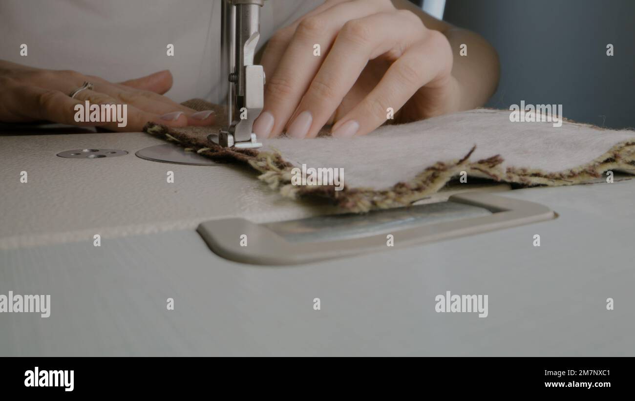 Mains de femme couturière travaille avec le tissu sur la machine à coudre. Une femme rade ses vêtements dans un atelier d'atelier ou à la maison. Concept de la mode, de l'industrie de la couture, de la main d'œuvre et de l'auto-emploi. Gros plan. Banque D'Images