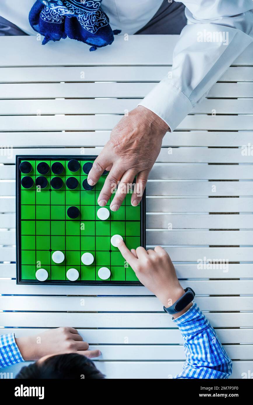 un grand-père montre à son petit-fils un jeu de société. La table est blanche et en bois. Banque D'Images