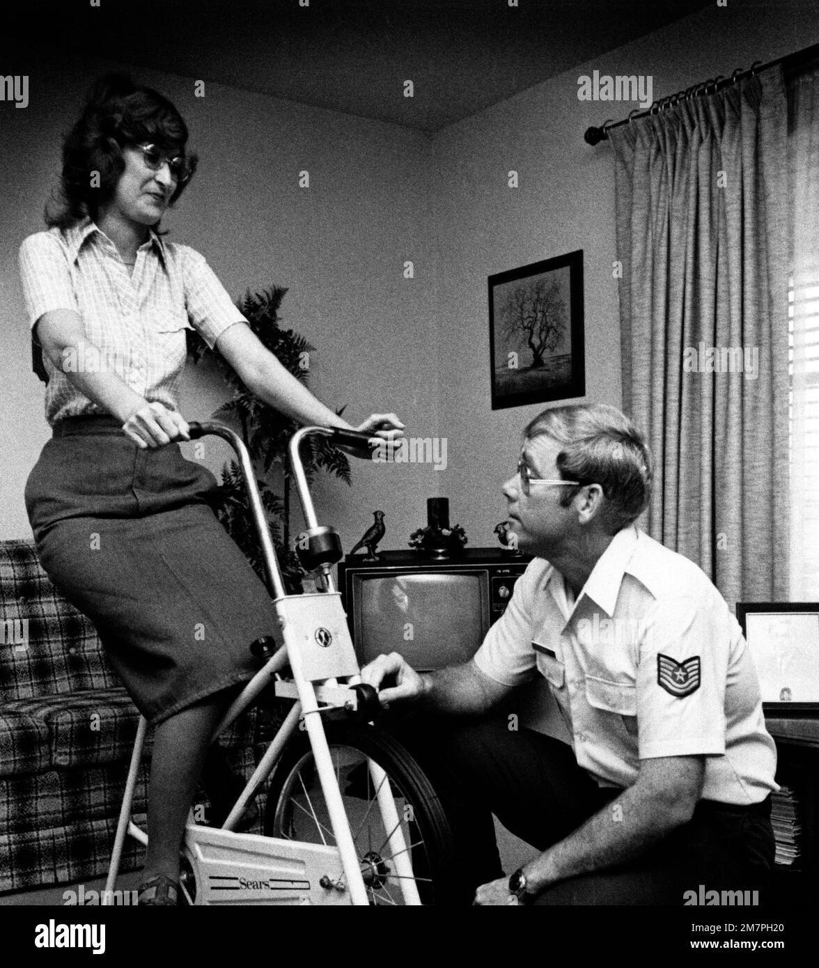 TSGT Bob King ajuste la tension sur le vélo d'exercice sa femme est pédalier. Katy King serait probablement morte aujourd'hui si elle n'avait pas eu de greffe cardiaque sur 4 avril 1975. Base: Fort Sam Houston, San Antonio État: Texas (TX) pays: États-Unis d'Amérique (USA) Banque D'Images