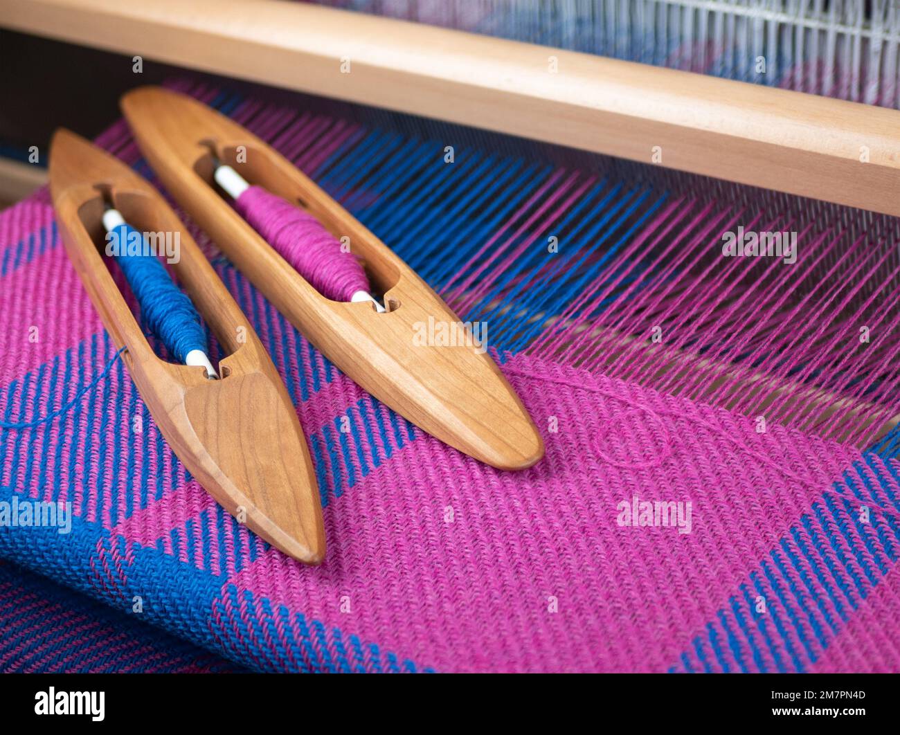 Deux navettes de bateau en bois avec des fils bleus et roses sur le métier à tisser de table, foyer sélectif. Concept de tissage de métier à tisser, création de tissu, fabrication Banque D'Images