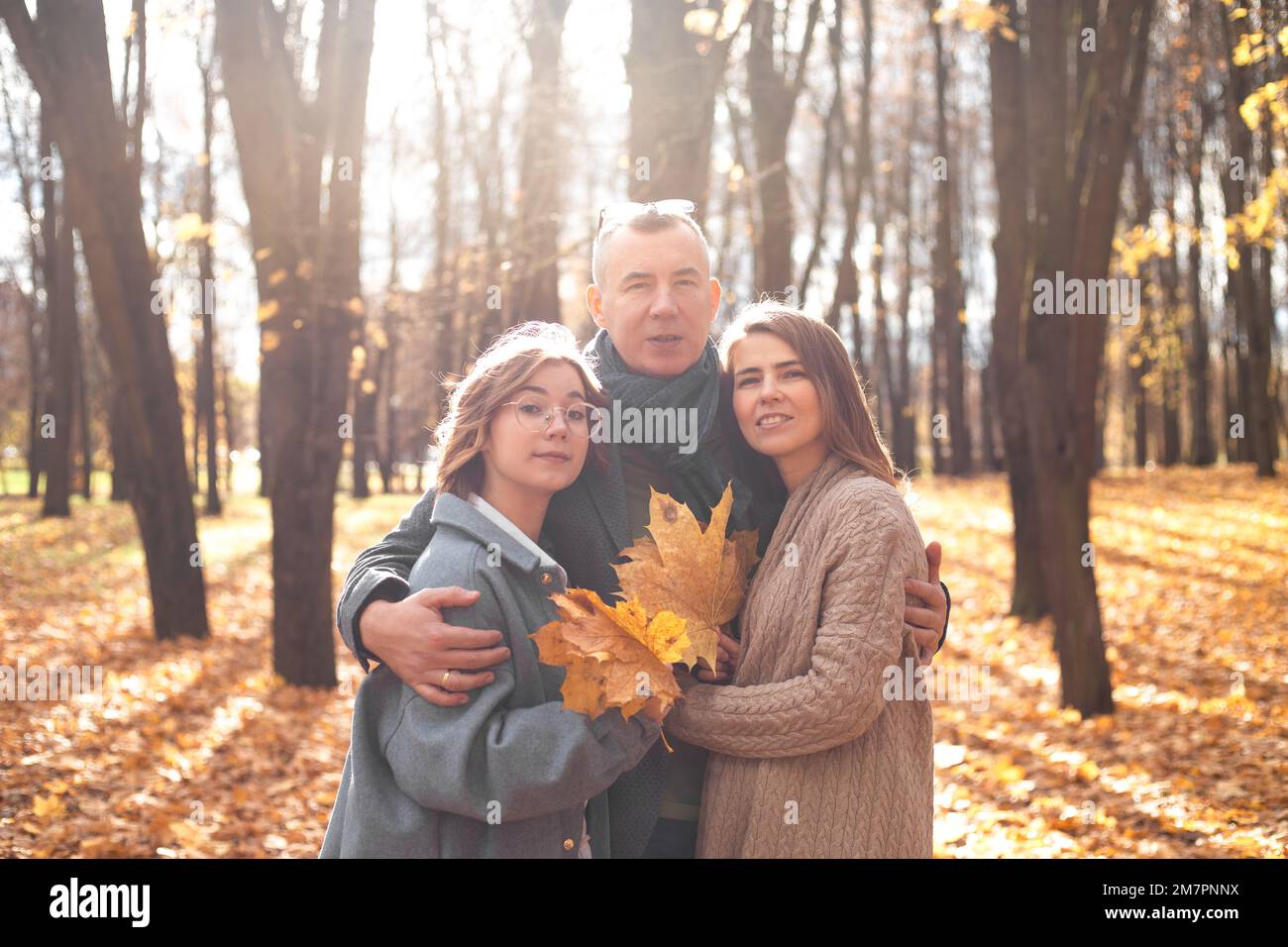 Portrait d'une famille heureuse de trois s'embrassant ensemble dans une forêt ensoleillée. Les parents et les adolescents marchent dans le parc d'automne. Banque D'Images