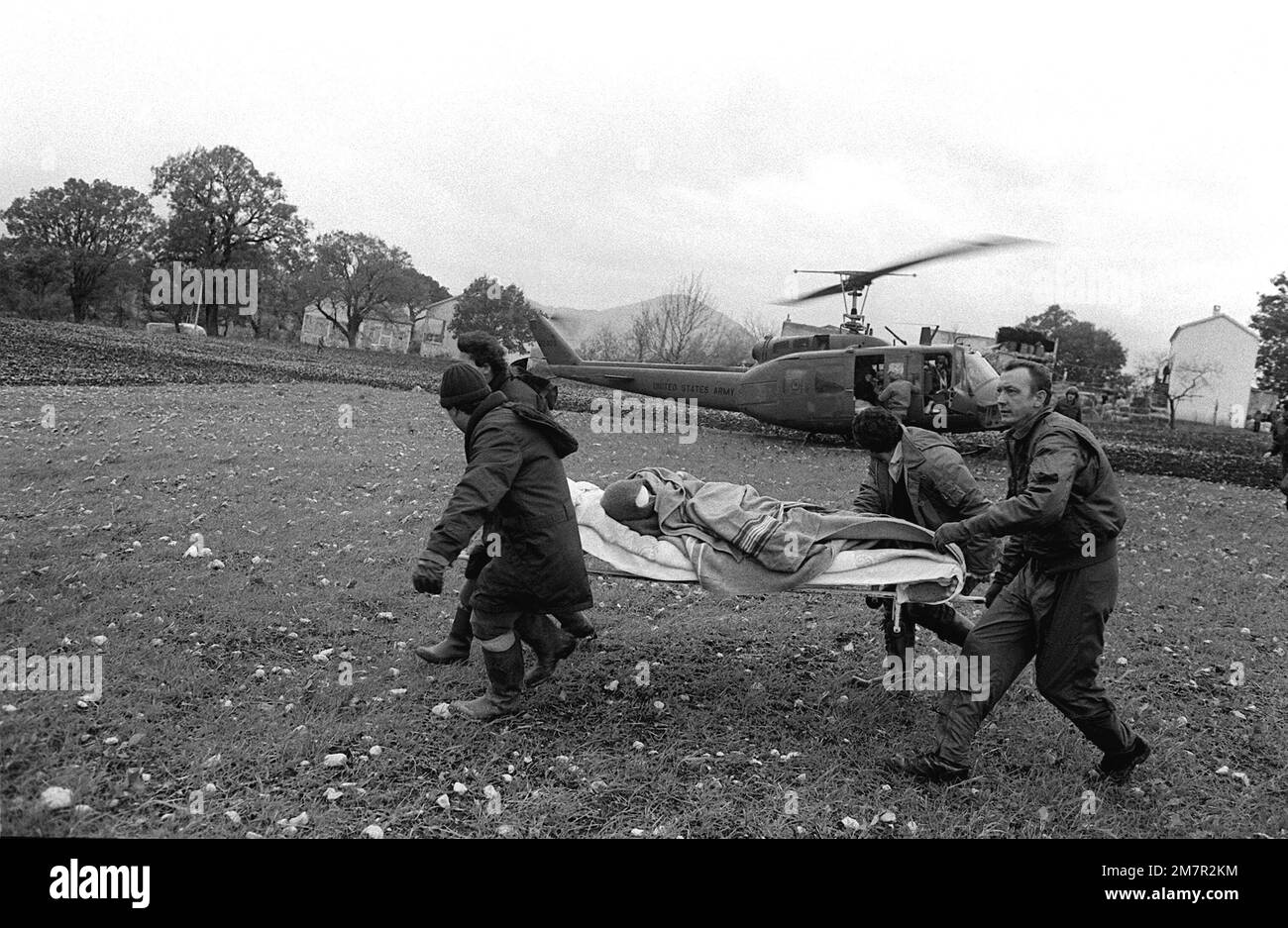 Un patient natif est transporté à un hélicoptère en attente (non visible) alors qu'un hélicoptère UH-1H Iroquois de l'armée (arrière-plan) se prépare au décollage. Le patient a été blessé lors d'un tremblement de terre majeur sur 23 novembre. Base: San Gregorio pays: Italie (ITA) Banque D'Images