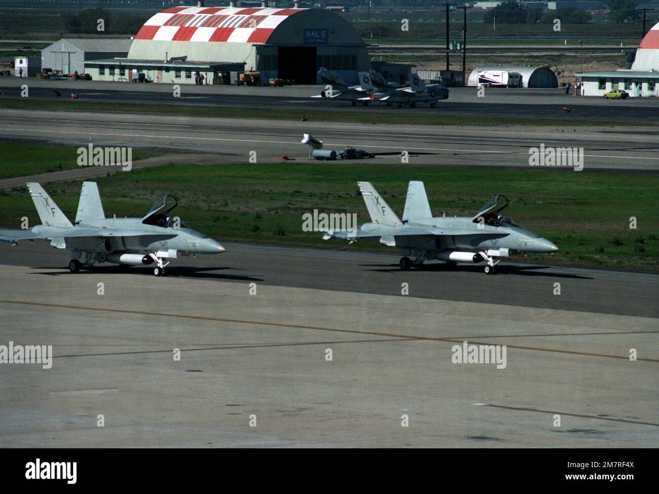 Vue de droite de deux avions F/A-18 Hornet de l'Escadron d'essai et d'évaluation aériens quatre (VX-4), stationnés sur la piste au Centre d'essai des missiles du Pacifique. Deux Avions Corsair II A-7, avec ailes rabattues, sont stationnés devant le hangar. Base: Naval Air Station, point Mugu État: Californie (CA) pays: Etats-Unis d'Amérique (USA) Banque D'Images