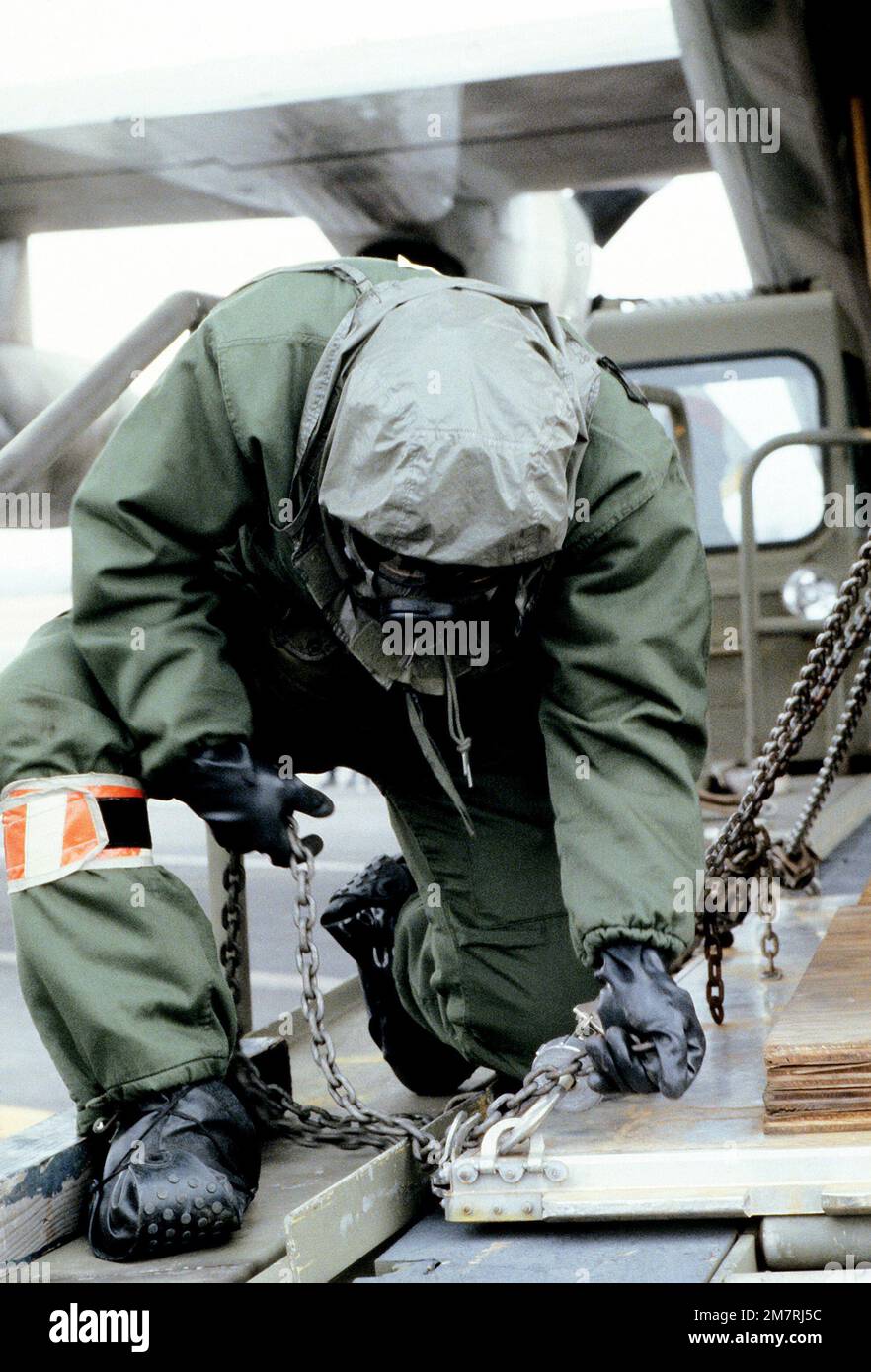 Un aviateur portant des vêtements de protection sécurise une palette avec des chaînes avant de la charger à bord d'un avion C-130 Hercules. L'aviateur est de l'aile du transport aérien militaire de 317th, Garde nationale aérienne, impliqué dans un exercice de guerre chimique. Base: Rickenbacker Ang État de base: Ohio (OH) pays: États-Unis d'Amérique (USA) Banque D'Images
