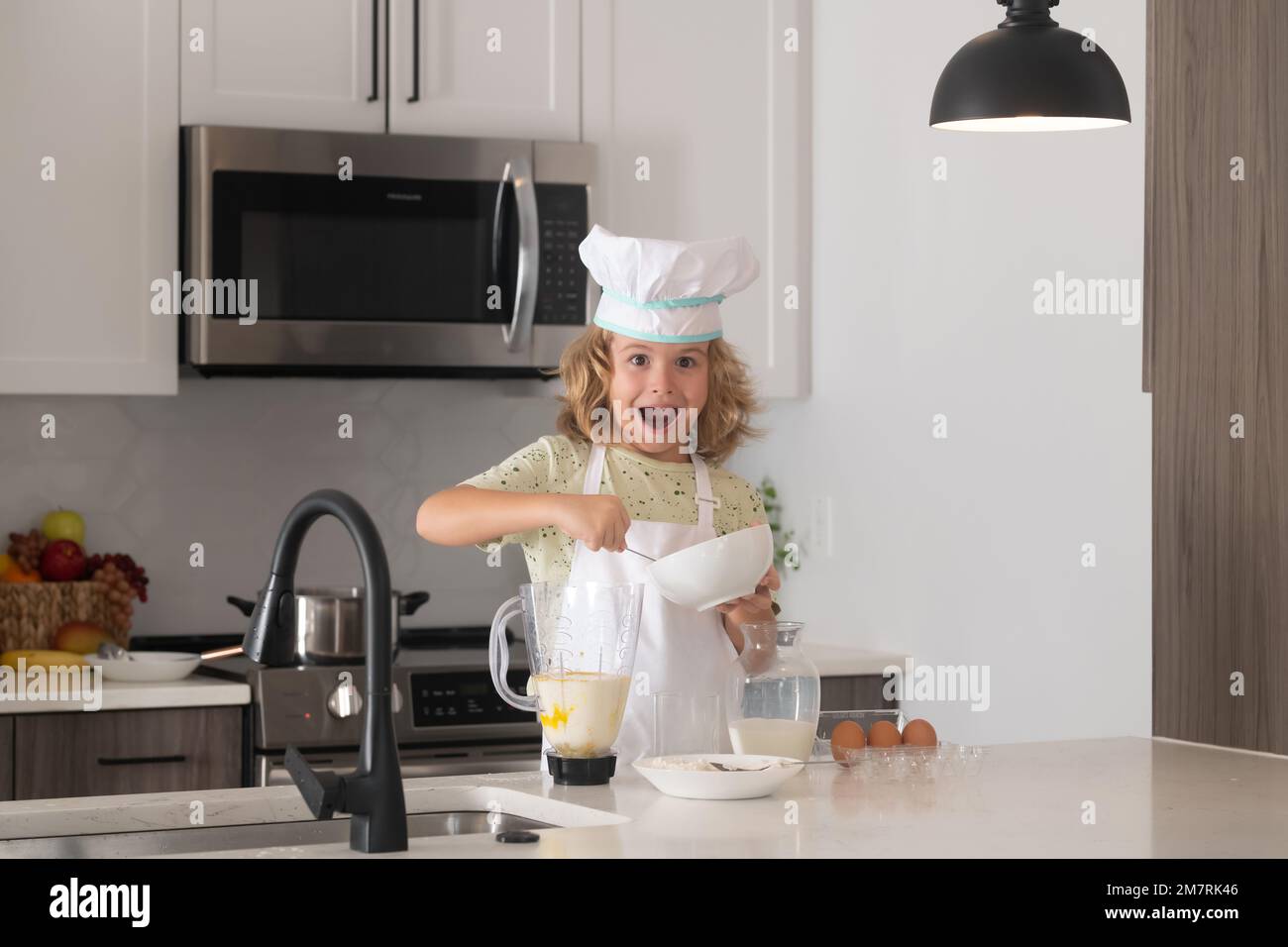 Chef enfant garçon cuisant sur la cuisine. Le chef cuisinier prépare la nourriture en cuisine. La cuisine des enfants. Un garçon de l'adolescence avec un tablier et un chapeau de chef préparant un repas sain. Banque D'Images