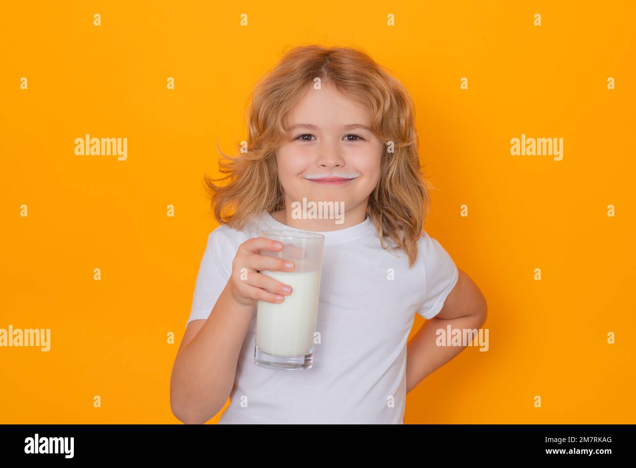 Un petit enfant boit du lait. Enfant avec un verre de lait sur fond jaune isolé. Banque D'Images