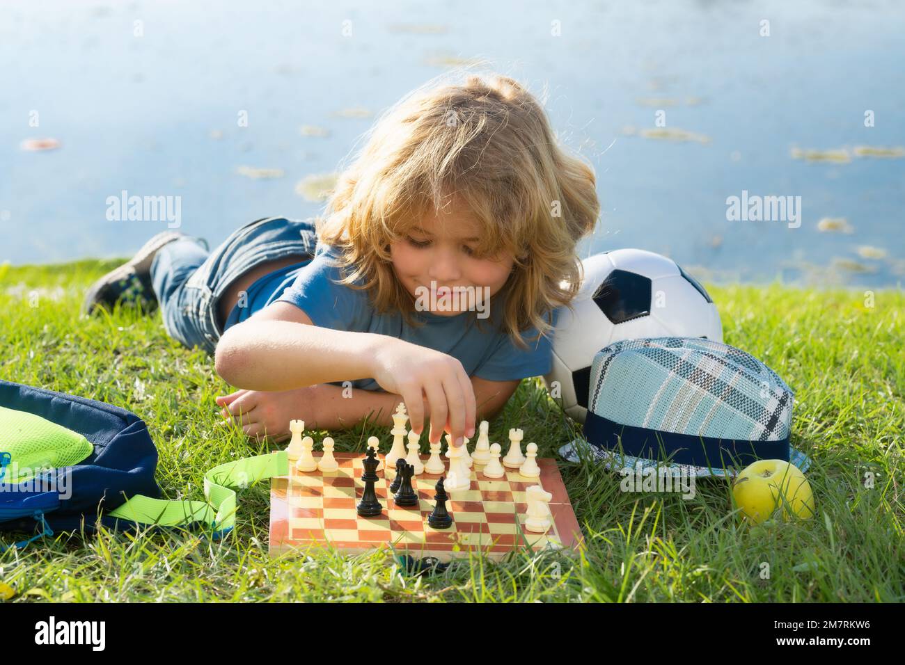 École d'échecs en plein air. Enfant penser ou planifier au sujet du jeu d'échecs, en posant sur l'herbe dans le parc d'été. Des écoliers intelligents, intelligents et intelligents. Banque D'Images