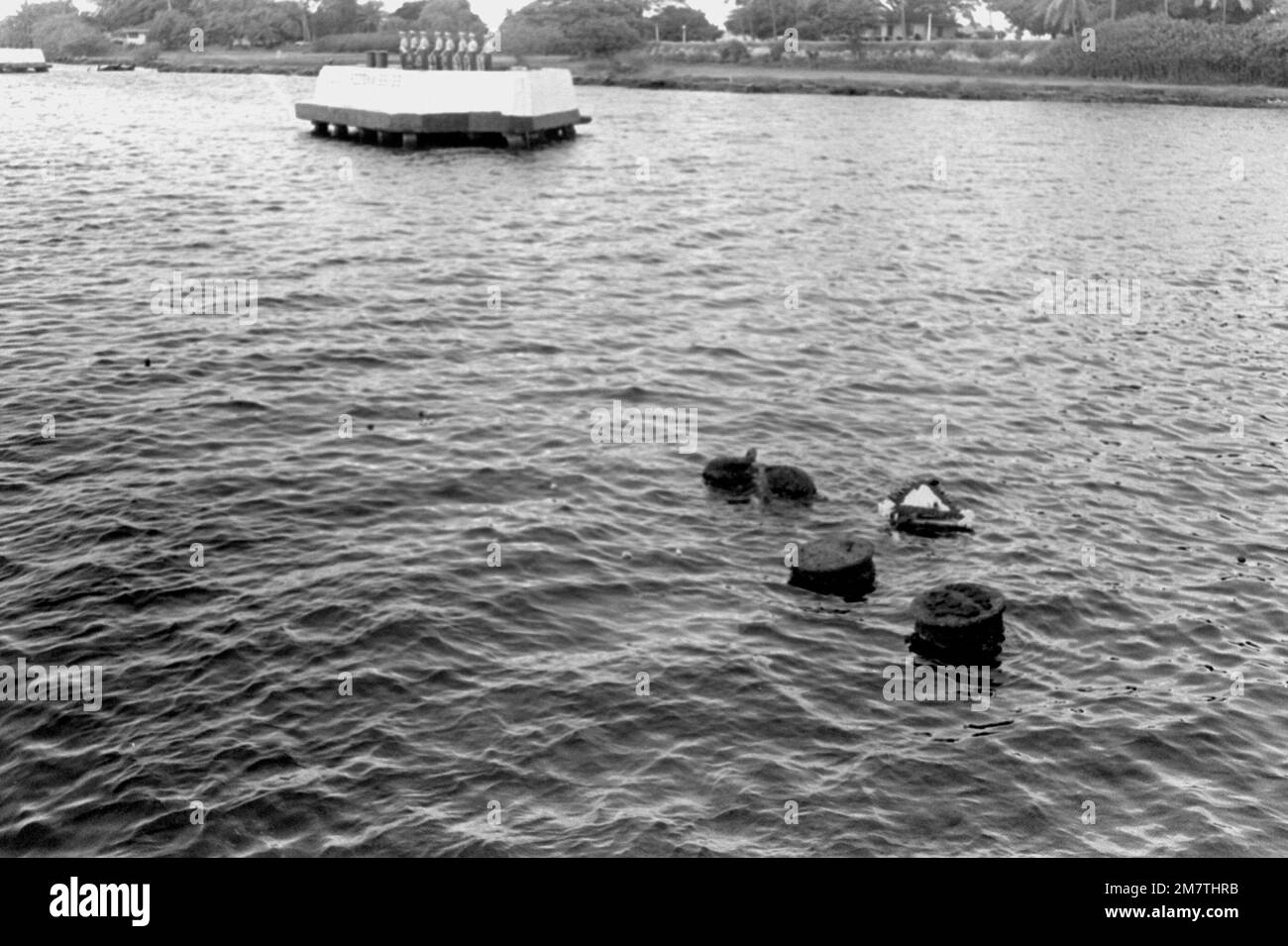 Des fleurs et une couronne flottent devant les morceaux d'amarrage du cuirassé USS ARIZONA (BB-39). En arrière-plan, un garde d'honneur marin attend sur un bloc d'amarrage pour tirer un hommage lors de la cérémonie commémorant le 40th anniversaire de l'attaque japonaise sur Pearl Harbor. Base: Pearl Harbor État: Hawaï (HI) pays: Etats-Unis d'Amérique (USA) Banque D'Images