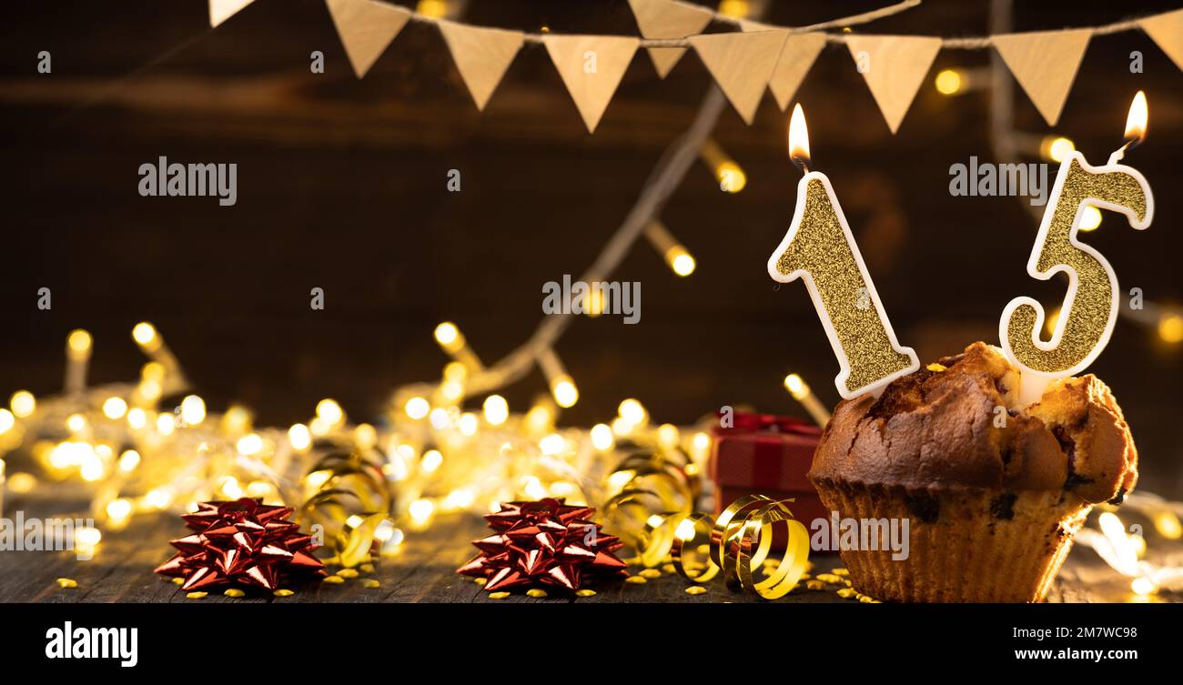 Bougie au feu d'or numéro 15 dans un cupcake sur fond de bois de célébration avec des lumières. Gâteau d'anniversaire. Copier l'espace. Bannière Banque D'Images