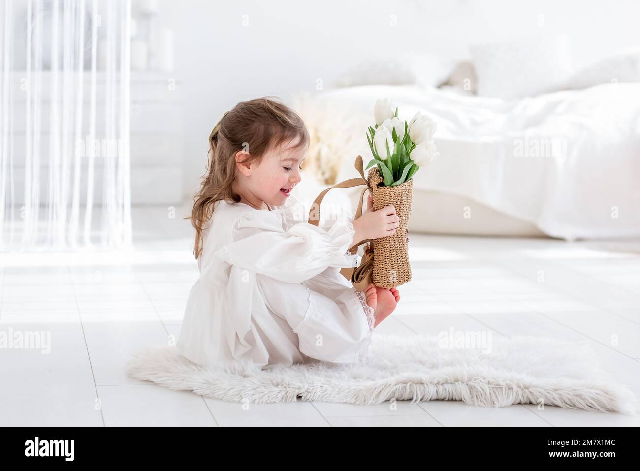 Portrait rapproché d'une petite fille dans une robe blanche, chemise de nuit. Le tout-petit embrasse un bouquet de tulipes blanches fraîches et délicates. Cadeau pour les vacances, le Banque D'Images