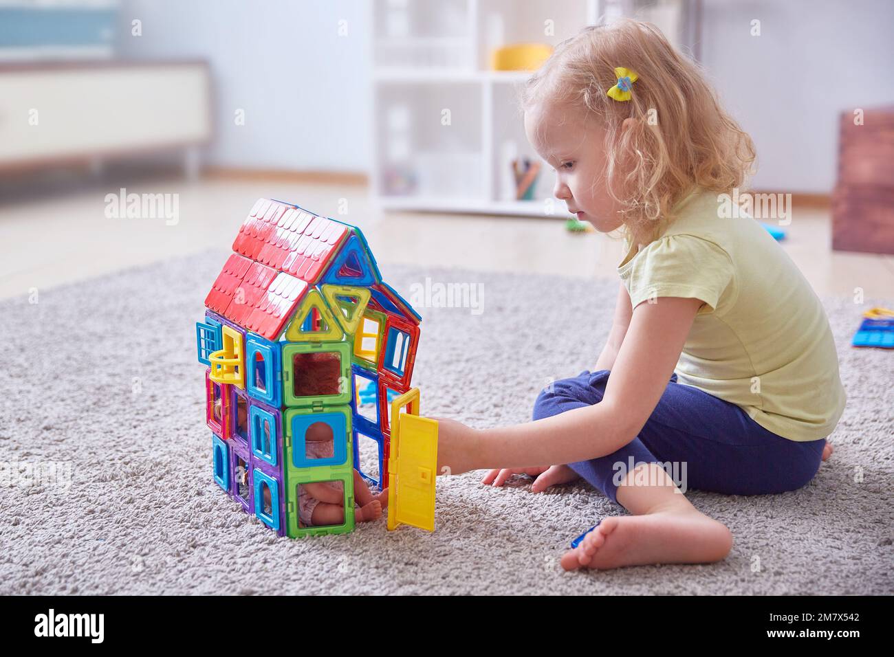 Un enfant aux cheveux bouclés recueille une maison faite de pièces de créateur colorées sur le tapis. Copier l'espace Banque D'Images