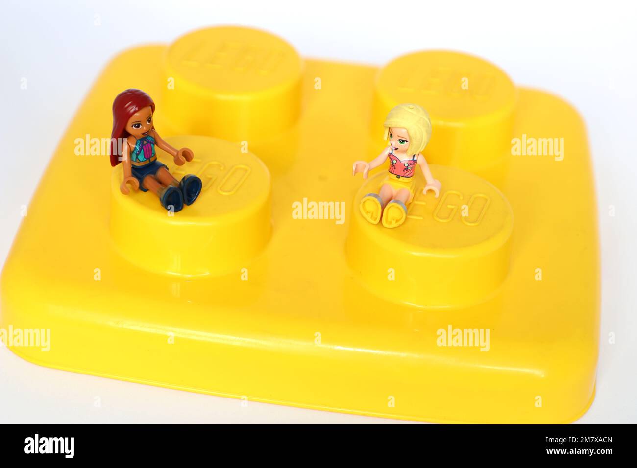 2 jeunes femmes lego à mini-figurine assises sur un bloc lego jaune géant. Utilisation éditoriale Banque D'Images