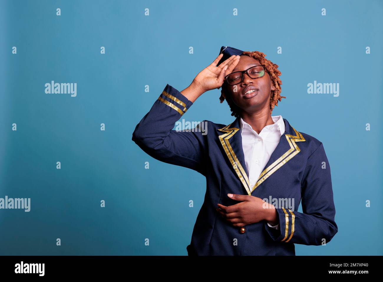 Une femme de bord a l'air fatiguée après un long itinéraire de vol international, avec la main sur le front souhaitant se reposer. Hôtesse portant un uniforme en studio, prise sur fond bleu. Banque D'Images