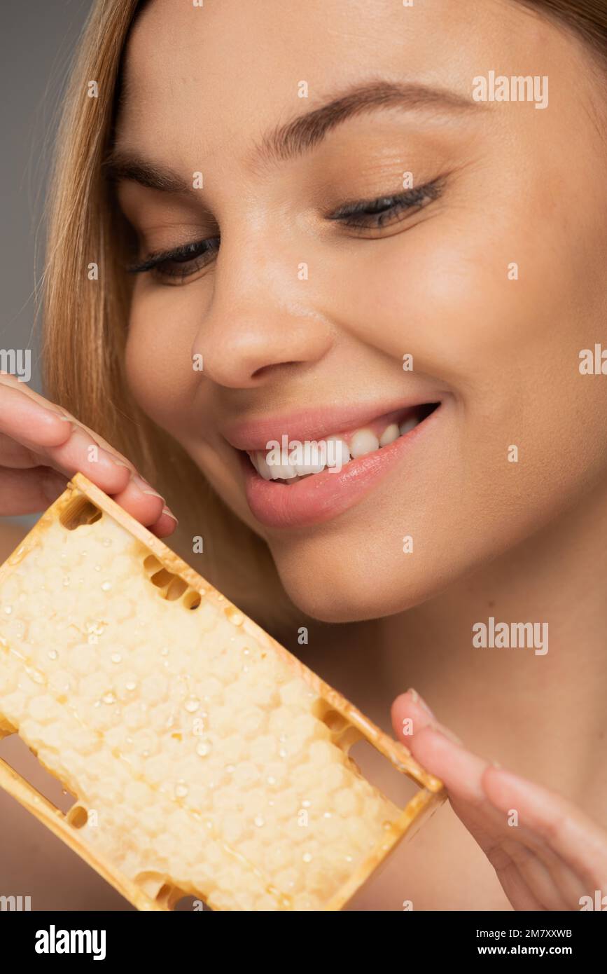 gros plan de la femme heureuse tenant le miel doux en nid d'abeille isolé sur gris, image de stock Banque D'Images