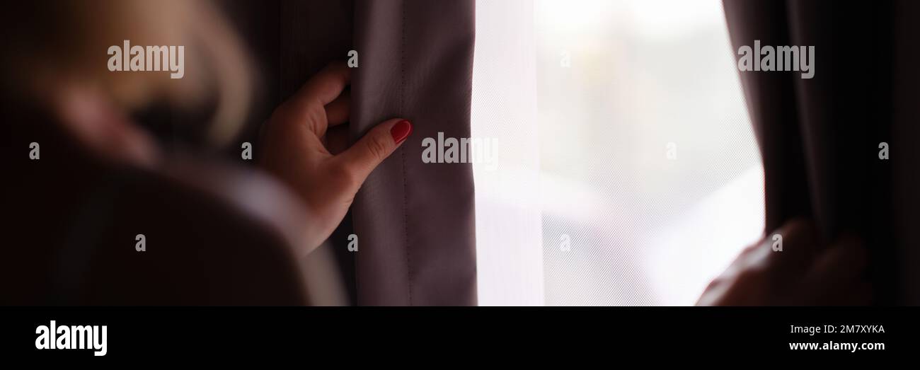 Une femme se tient à la fenêtre et ouvre les rideaux vue arrière Banque D'Images
