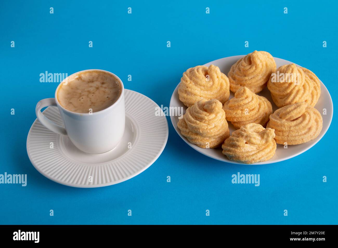 photographez une tasse de café sur une soucoupe et un peu de meringue sur une assiette sur fond bleu Banque D'Images