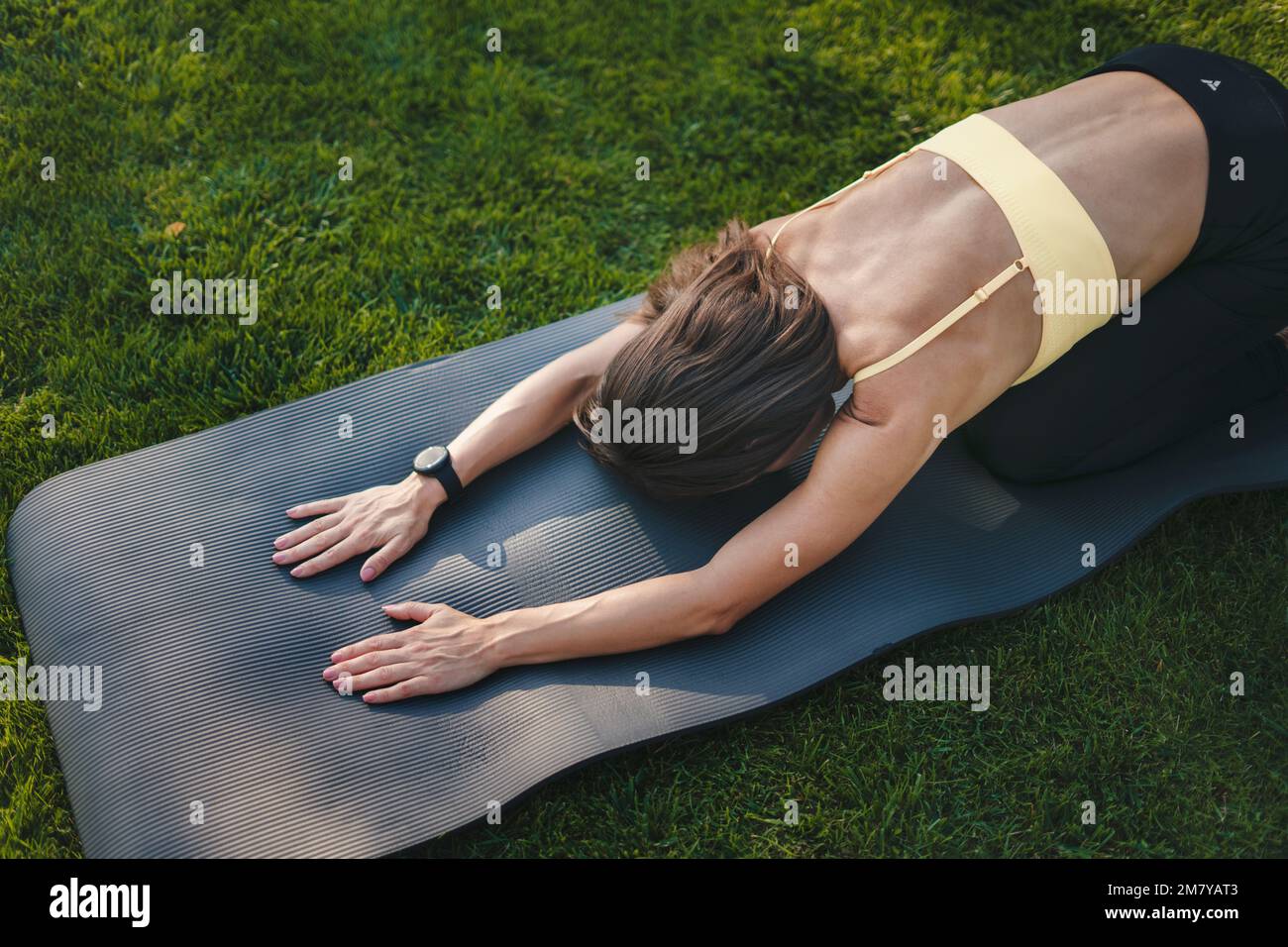 Vue de dessus d'une femme sportive qui la stretse le dos avant d'autres exervices, assis sur un tapis de yoga en plein air. Effet d'éblouissement par le soleil. Un style de vie heureux Banque D'Images