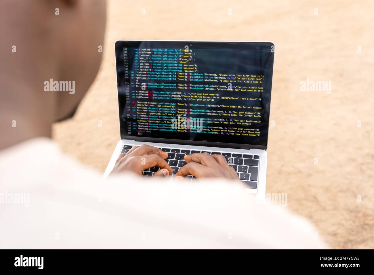 D'en haut anonyme homme indépendant noir dactylographiant sur le clavier d'ordinateur portable et d'écrire du code tout en passant du temps sur la plage de sable en journée Banque D'Images